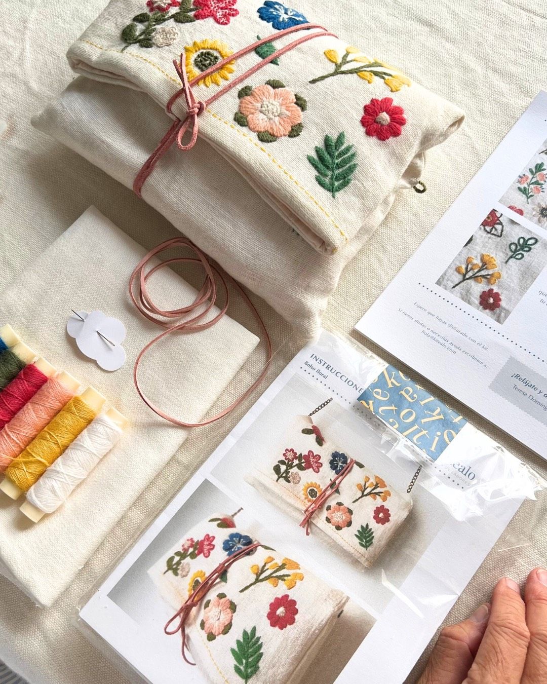 Materiales del kit de bordado clutch: hilos de lana, aguja, diseño floral y tela de lino.